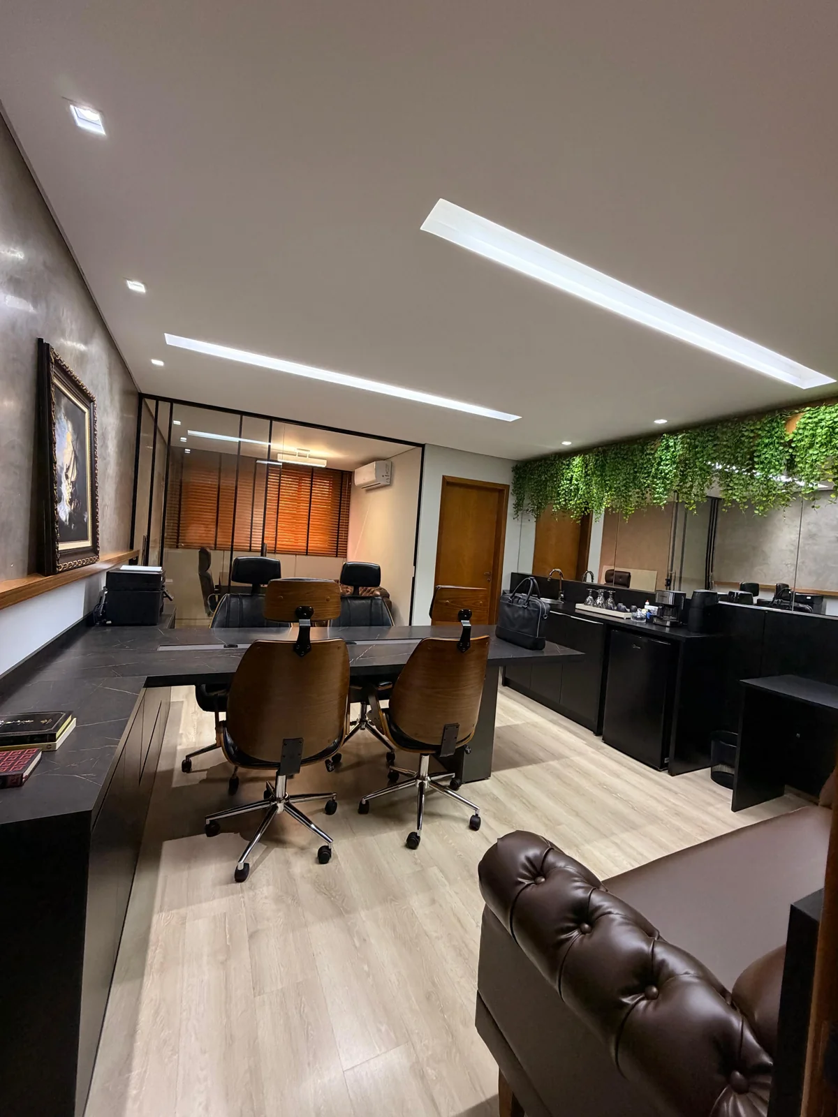 Vista do escritório com mesas de atendimento, poltronas e sala reservada ao fundo
